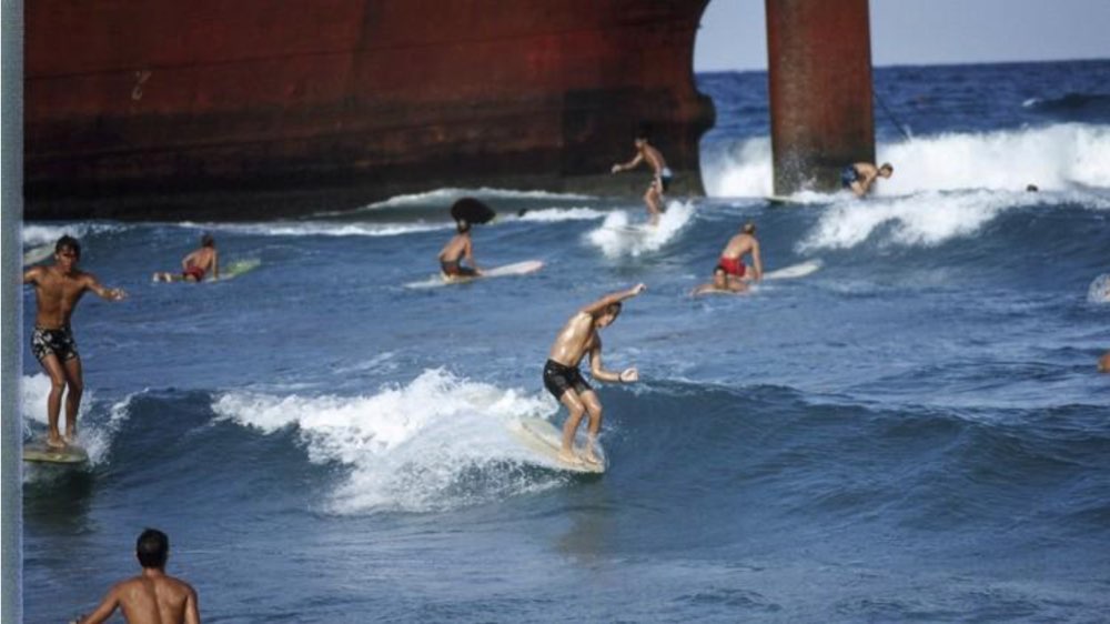Surfers riding waves beside the grounded freighter Amaryllis, Singer Island, 1966